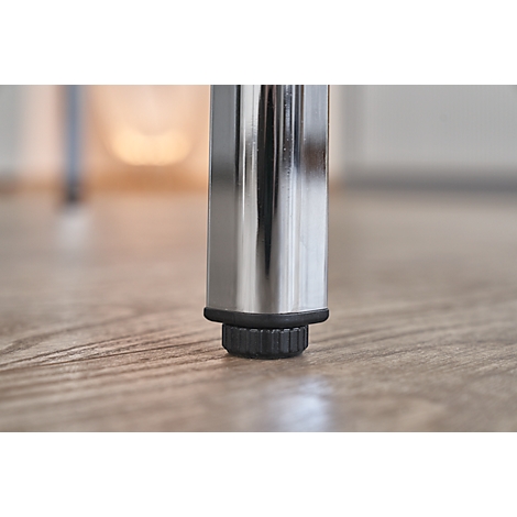 Close-up of a chrome table leg standing on a wooden floor. The foot of the leg is made of black plastic.