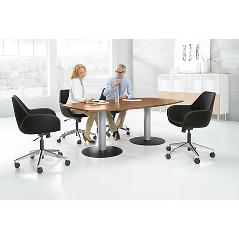 Two people sit at a table surrounded by office chairs. Large windows in the background.