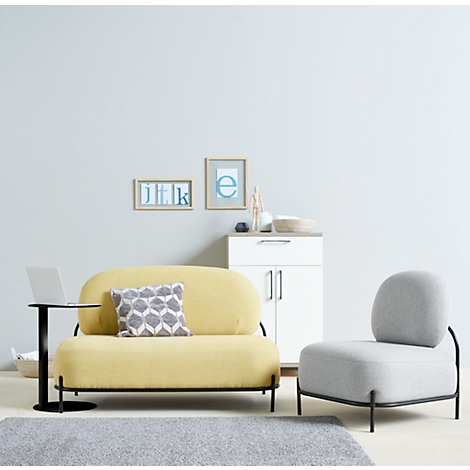 Sofá amarillo con cojines grises, junto a un sillón gris, un portátil sobre una mesa auxiliar negra.