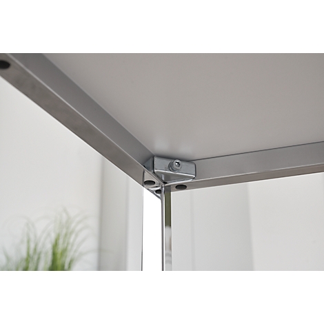 Primer plano: Esquina de una mesa, estructura de metal plateado, material de la encimera blanco, tornillos y conexiones.