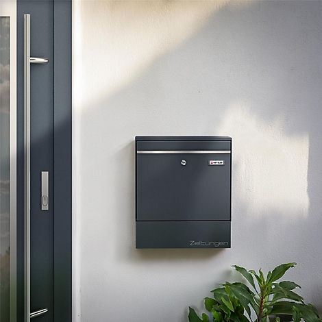 Dunkelgrauer Briefkasten an Hauswand. Unterhalb steht "Zeitungen".