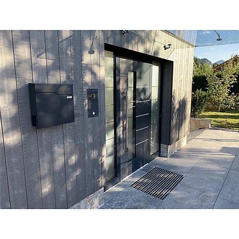 Moderne Haustür mit Klingel und Briefkasten in anthrazit. Der Boden besteht aus grauen Fliesen, im Hintergrund ist ein Garten zu sehen.