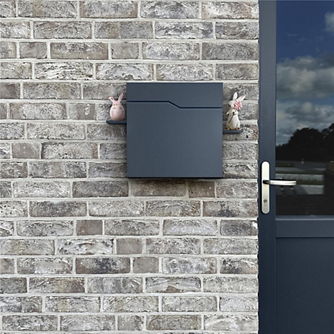 Dunkelgrauer Briefkasten an Backsteinmauer. Zwei Hasenfiguren schmücken ihn.