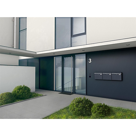 Moderne gevel met huisnummer 3 en brievenbussen. Gazon en struiken voor het huis. Grote glazen voorkant met entreedeur.