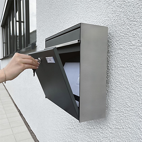 Grijze aan de muur gemonteerde brievenbus met open klep, een arm met sleutel die hem opent. De brievenbus hangt aan een witte muur.