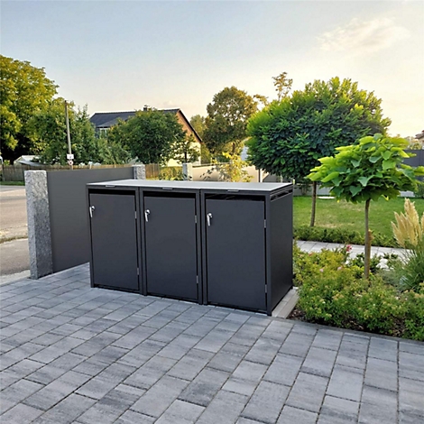 Trois boîtes noires pour poubelles sur des pavés, entourées d'espaces verts et d'arbres.