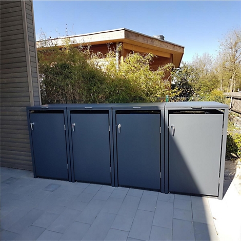 Poubelles grises sur dalles de pierre, derrière des buissons et une maison.