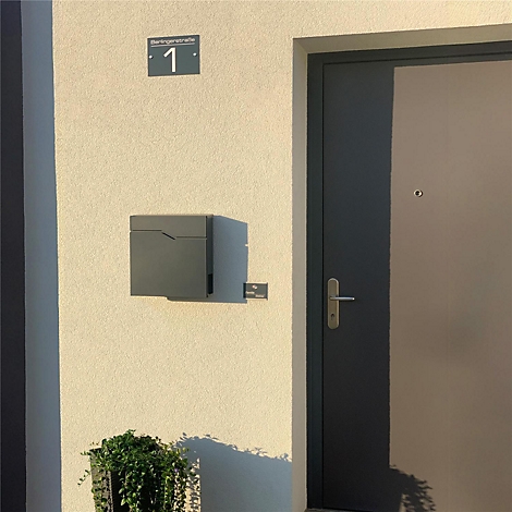 Grijze brievenbus aan de muur van het huis. Daarnaast huisnummer 1. Deur rechts met handvat.