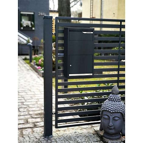 Schwarzer Briefkasten an einem Zaun im Freien, Buddha-Statue im Vordergrund.