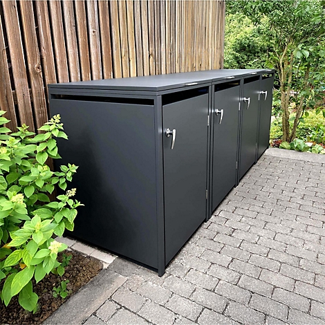 Drie grijze vuilnisbakken in de tuin, voor een houten wand en struiken. Handvatten en klinkers.