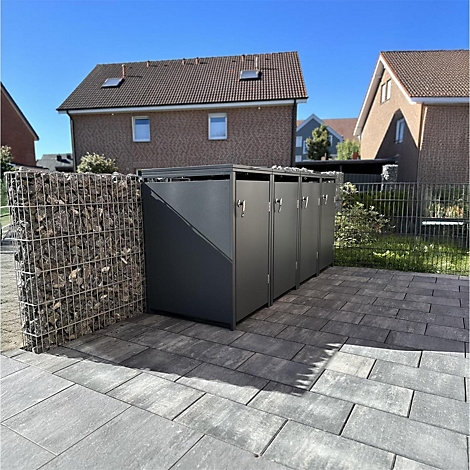 Donkere afvalbakken op stenen platen voor woongebouwen, links een stenen muur.