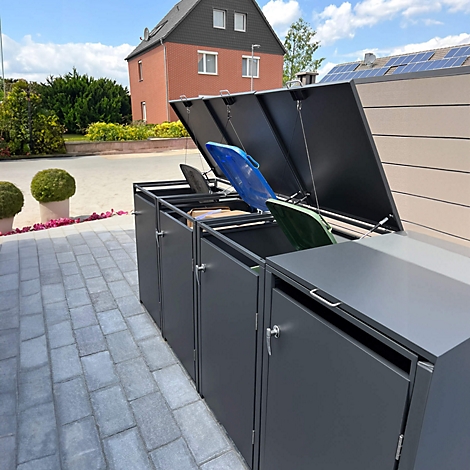 Graue Mülltonnenboxen mit geöffneten Deckeln. Blaue, grüne und schwarze Mülltonnen sind sichtbar. Haus im Hintergrund.
