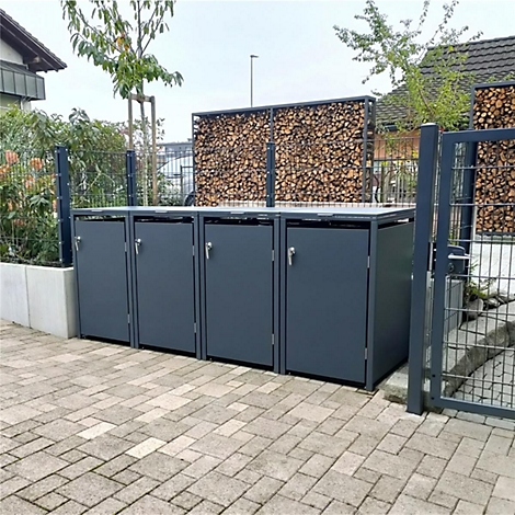 Graue Mülltonnenboxen auf Pflastersteinen, im Hintergrund Holzwand und Zaun.