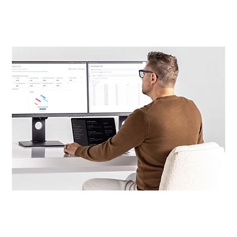 Ein Mann mit Brille sitzt am Schreibtisch und arbeitet an einem Computer. Auf dem Tisch stehen zwei Monitore und ein Laptop.