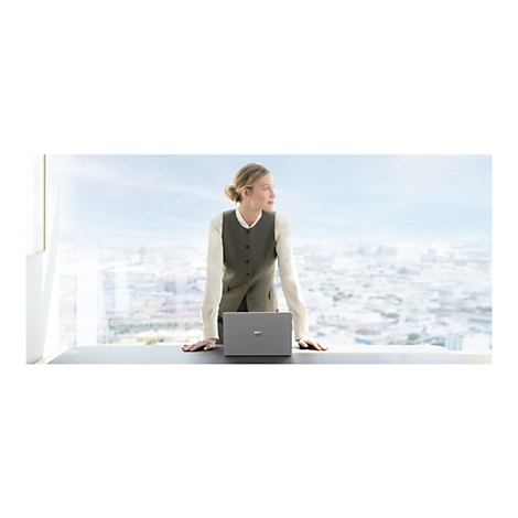 Eine Frau im BÃ¼ro, steht an einem Fenster und blickt auf die Stadt. Auf dem Tisch liegt ein Laptop.