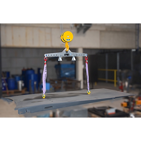 Industriële hijsinstallatie die een metalen plaat optilt, bevestigd aan een gele katrol.