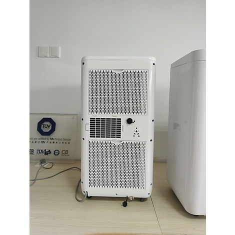 Achterkant van een witte draagbare airconditioner met ventilatieopeningen. Daarnaast een ander wit apparaat. Op een tafel en muur.