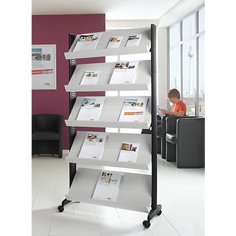 Presentation stand with brochures, behind it a boy is reading a magazine.