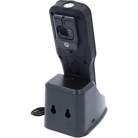 Schwarze LED-Arbeitsleuchte mit Ladestation. Oberhalb leuchtet eine helle Lampe, darunter befindet sich ein Clip.