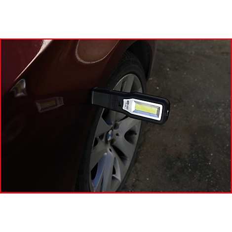Eine schwarze LED-Arbeitsleuchte ist an einem roten Autokotflügel befestigt. Im Hintergrund ist ein Reifen und die Felge zu sehen.