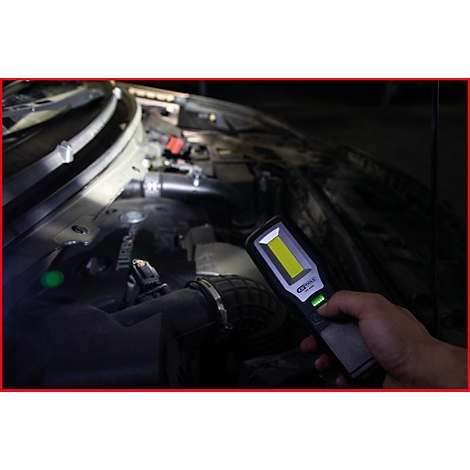 Nahaufnahme einer Hand, die eine Stablampe im Motorraum eines Autos hält. Die Lampe leuchtet das Innere aus.