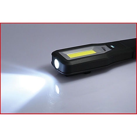Eine schwarze Stablampe leuchtet auf hellem Untergrund. Das Licht der LED ist gut sichtbar.