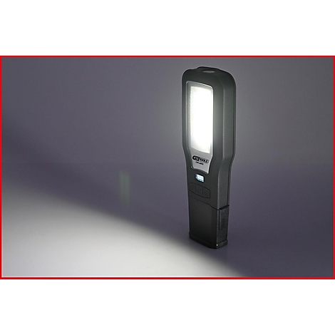 Eine schwarze LED-Werkstattlampe leuchtet hell. Sie steht auf einer schrägen Fläche. Ein weißer Lichtkegel wird auf eine graue Oberfläche geworfen.