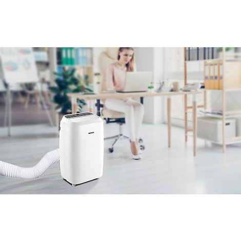 Ein weisser mobiler Klimaanlage steht im Büro. Im Hintergrund sitzt eine Frau an einem Schreibtisch.