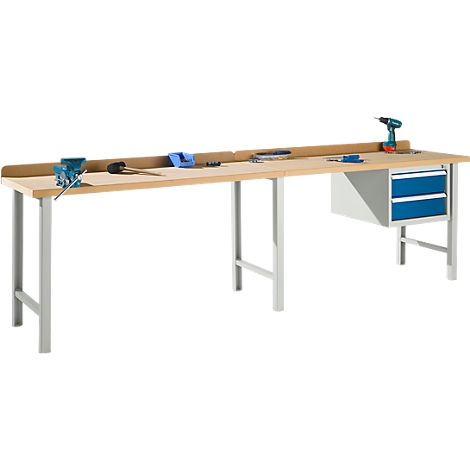 A light-colored workbench with silver legs, tools, and drawers. Drill, vise, hammer, wrench.