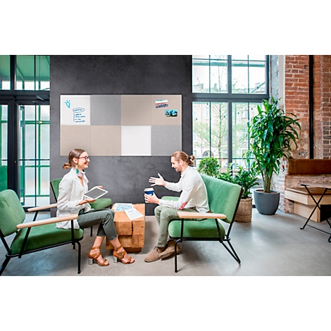 Deux personnes assises dans des fauteuils discutent devant un tableau d'affichage. Les deux ont une boisson à la main.