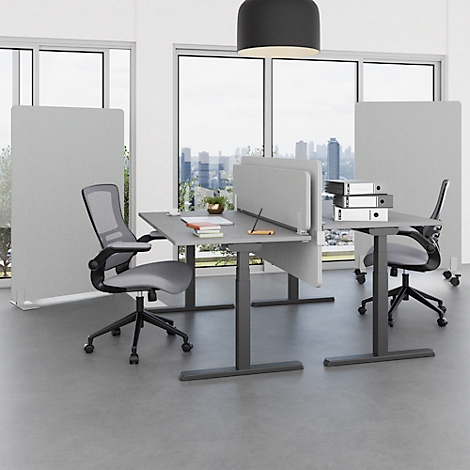 Kantoorruimte met tafels en stoelen. Grijze tafels met privacyschermen, stoelen met wieltjes. Grote ramen met skyline.