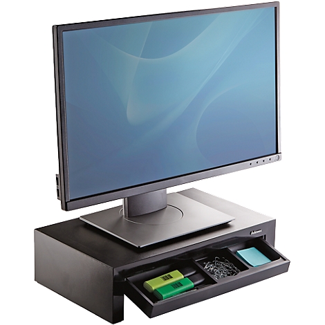 A black monitor stand with a drawer, on which a screen stands, there are pens and paper clips in the drawer.