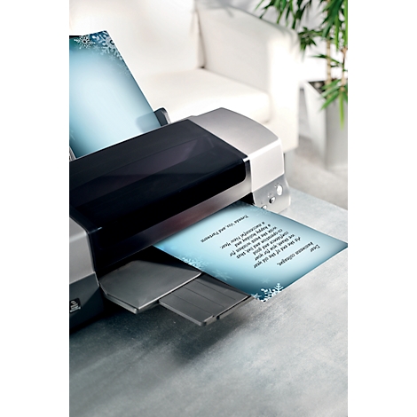 A printer is printing a letter, which is lying on a table. In the background are a sofa and a plant.