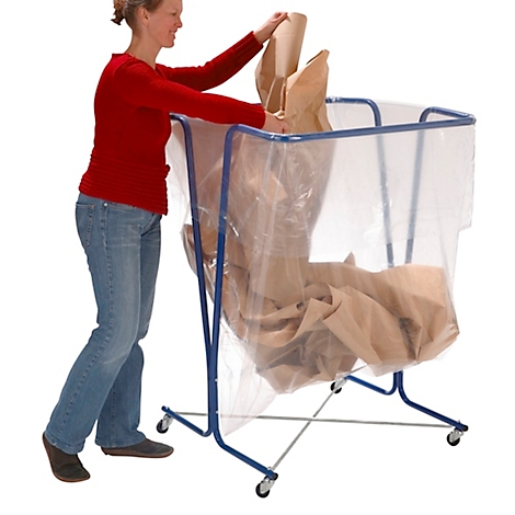 Een vrouw in spijkerbroek en een rood shirt plaatst bruin papier in een blauwe container met wielen en een plastic zak.