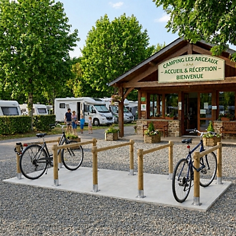 Ein hölzerner Fahrradständer vor dem Rezeptionsgebäude eines Campingplatzes mit Wohnmobilen im Hintergrund.
