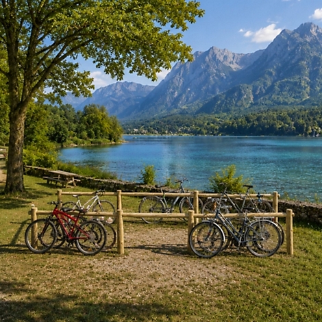Mehrere Fahrräder stehen an einem Holzständer vor einem malerischen Bergsee bei sonnigem Wetter.
