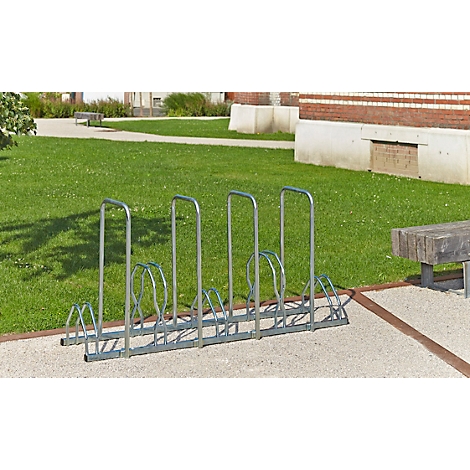 Metalen fietsenrek op verharde ondergrond, daarachter gazon, gebouw.