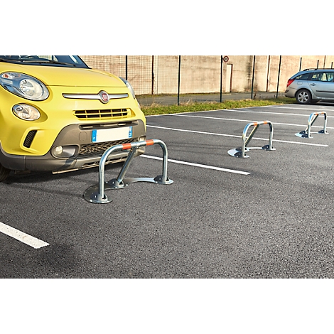 Yellow car parking behind parking barrier. In front, a second barrier, behind which parking bays are marked. Grey asphalt.