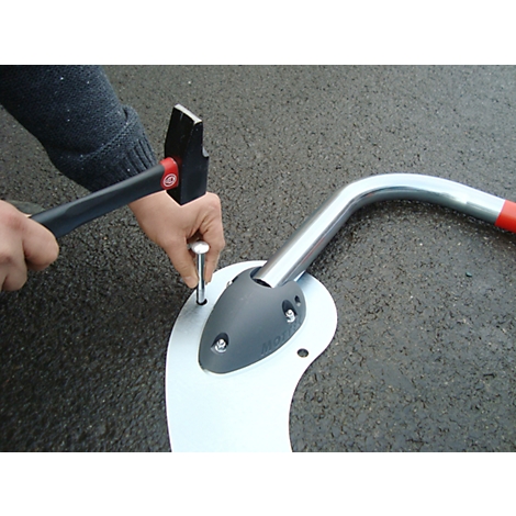 Person hammers a nail into a metal plate. Next to it is a curved metal tube with a red tip.