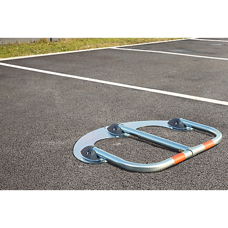 Metal parking barrier on asphalt. Silver, with orange stripes and black rubber feet attached.