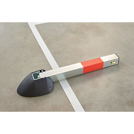 A gray parking barrier system lies on a concrete floor. The bar is silver, has a red stripe and a black foot.