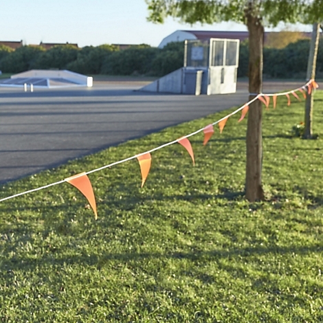 Orange pennant string in front of a skate park, lawn and trees.