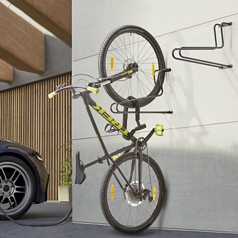 Ein schwarzes Mountainbike hängt vertikal an einer hellen Garagenwand in einem Wandhalter.