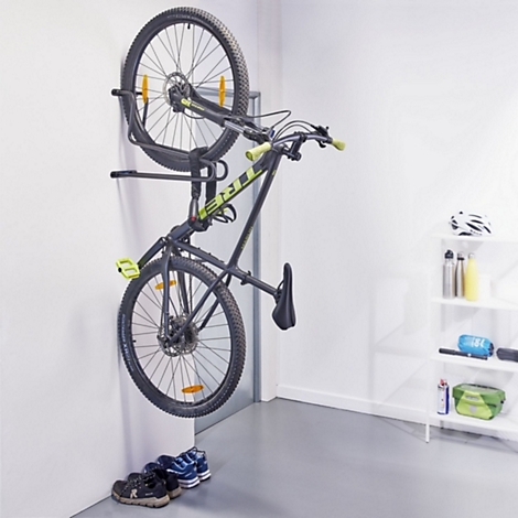 Ein schwarzes Mountainbike hängt platzsparend vertikal an einer Wandhalterung in einem weißen Raum.