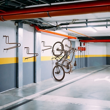 Ein Mountainbike hängt an einer Wandhalterung in einer Parkgarage mit weiteren leeren Wandhalterungen.