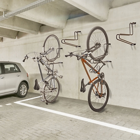 Zwei Fahrräder hängen in einer Tiefgarage an schwarzen Wandhalterungen.