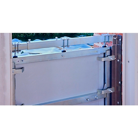 Detailopname van een zilveren overstromingsbeschermingsdeur die in een deurkozijn is gemonteerd. Schroeven en beugels bevestigen de deur.