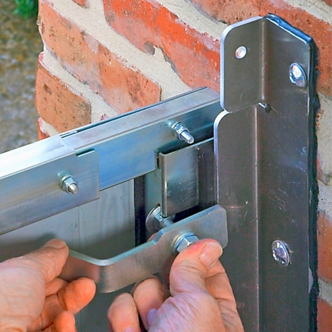 Handen houden metalen fitting op bakstenen muur. Fitting is op constructie geschroefd.