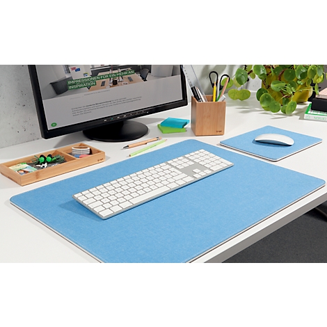 Desk with blue felt pad, keyboard, and mouse. In the background, a monitor with a website. Right: wooden cup, plant.
