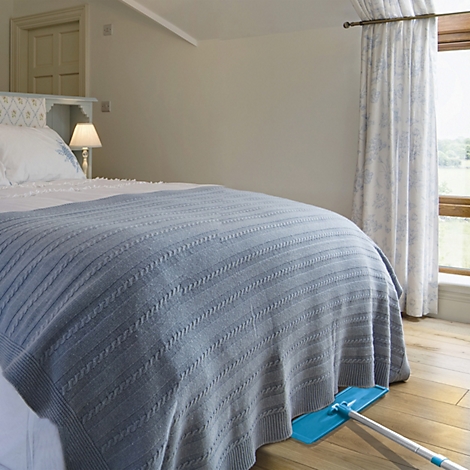 Blaues Bettlaken bedeckt Bett. Blauer Wischer liegt auf Holzfussboden.